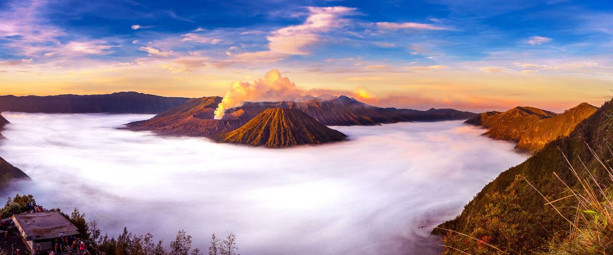 A mountain range with a cloud forest at its base and a small settlement on the left.