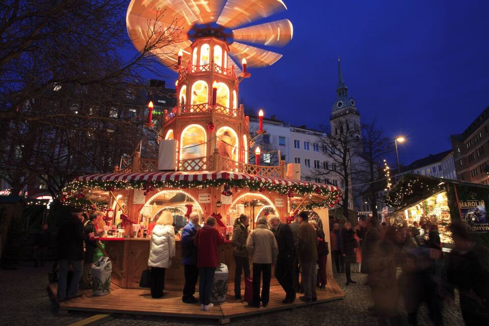 A festive market with a traditional wooden structure, a clock tower, and people gathered around.