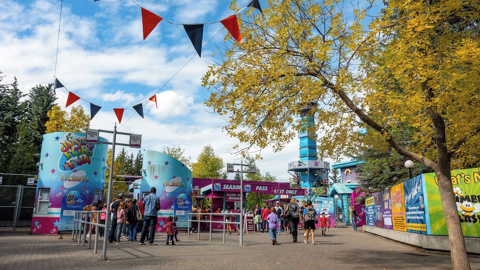 A theme park entrance with ticket booths, a seasonal pass booth, and a colorful fence.