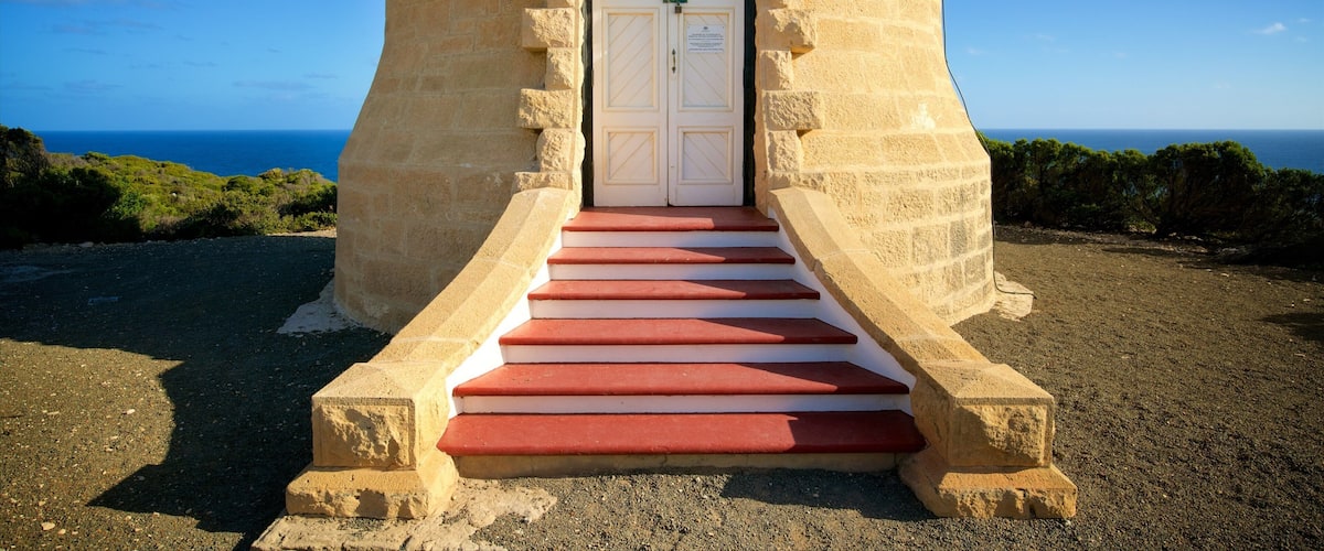 A stone tower with a white door and red steps leading up to it, overlooking a coastal landscape.