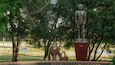 A statue of a man and a child in a park with trees and a sign in the background.