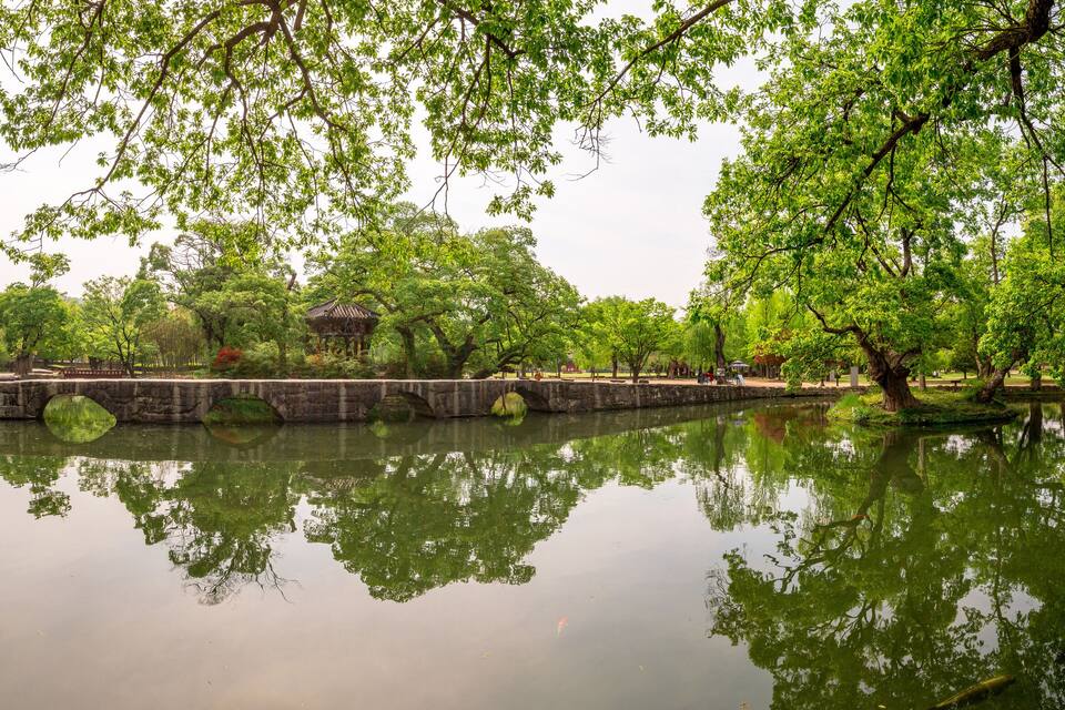 A serene pond surrounded by lush trees and traditional architecture.