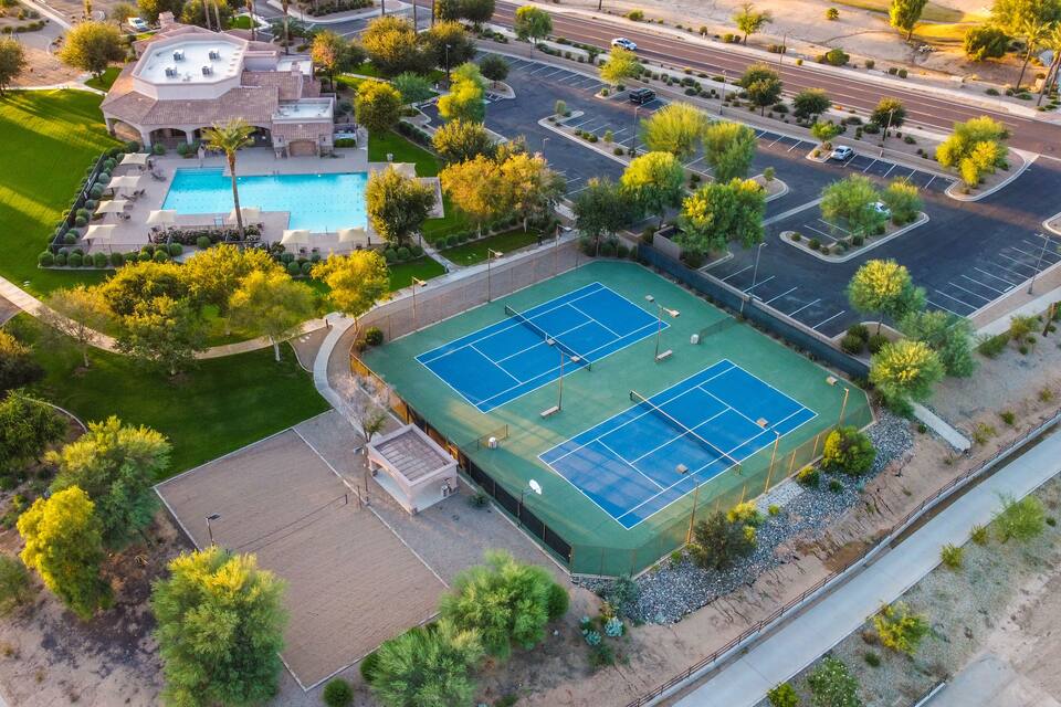 Vue aérienne d’un quartier résidentiel avec un court de tennis, une piscine et des jardins aménagés.