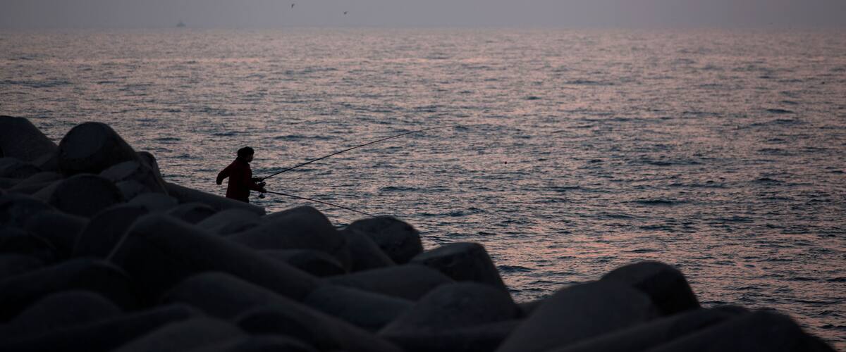 Sunset view with the silhouettes of fishing people on the seawall
