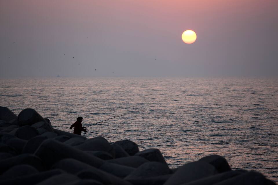 Un sol ponent sobre l'oceà amb roques al primer pla.