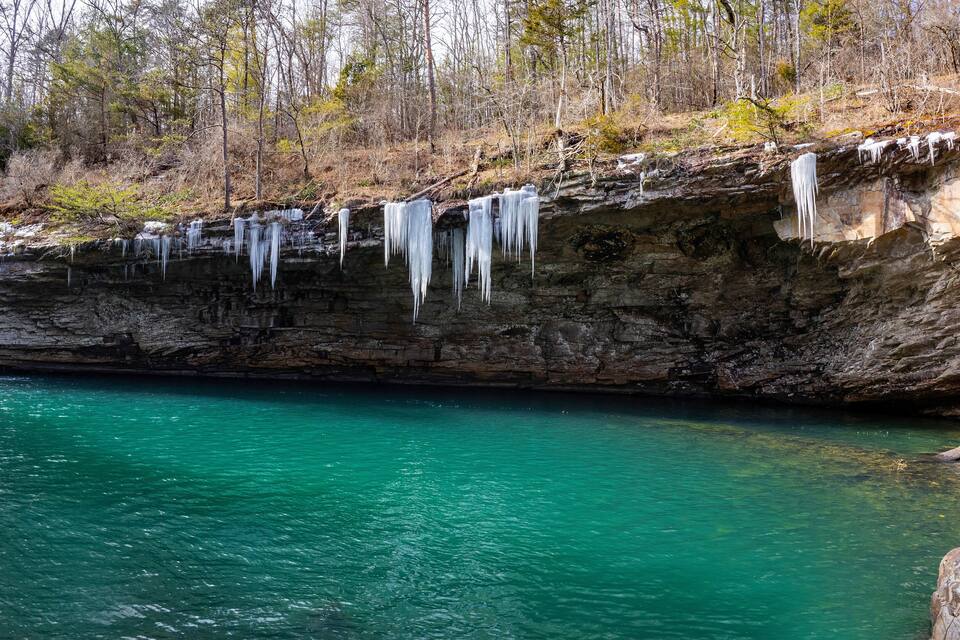 A rocky cliff with icicles hanging over a turquoise river.