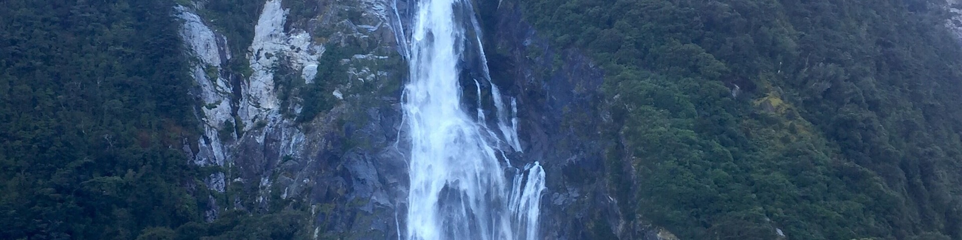 Milford Sound is a cliche must do for a good reason - it's awesome!! (Although I might like Doubtful sound "better". At least in comparing the actual sounds or fjords as they actually are). The upside to Milford - the drive there is beautiful and in Milford you can also kayak and check out the underwater observatory... Ooo and you get to go under Stirling Falls, which was amazing! 
This is Bowen falls which is the other permanent waterfall in Milford Sound. 
The day I was there was so sunny, and it was beautiful, the guides even said they never see it that clear and sunny! However, Milford is supposed to be even more magical in the rain because then hundreds of small waterfalls appear everywhere. The one time rain would've been good! Lol