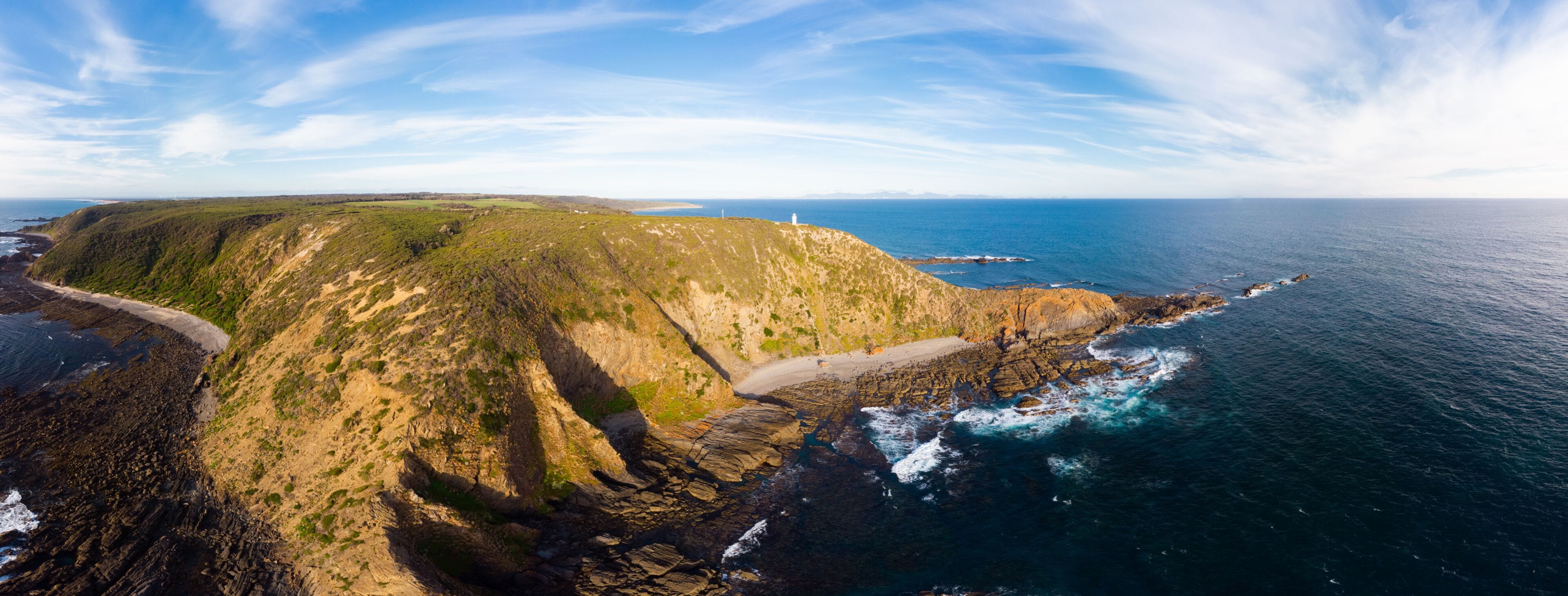 A coastal landscape with a lighthouse, rocky cliffs, and a beach.