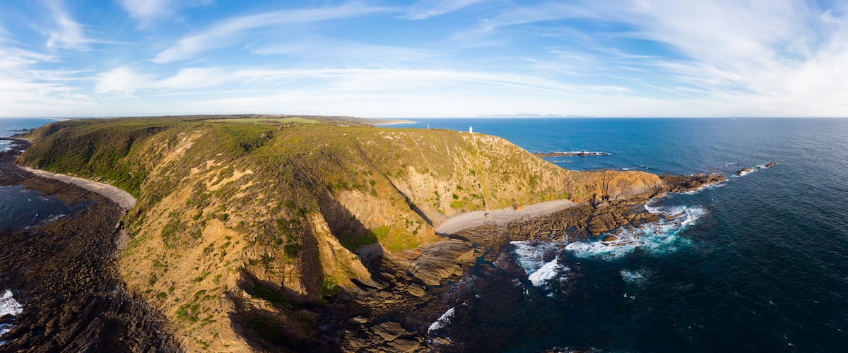 A coastal landscape with a lighthouse, rocky cliffs, and a beach.