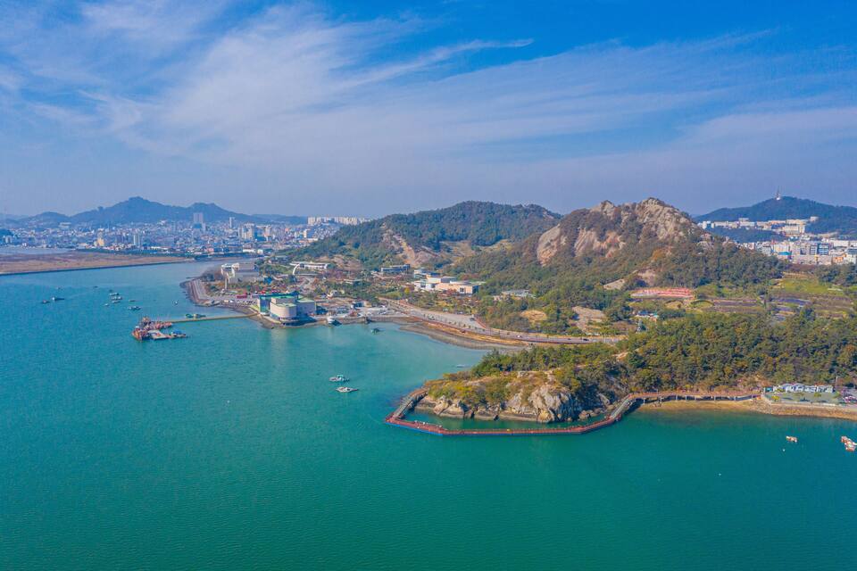 A coastal cityscape with a bay, boats, and a prominent hill with buildings.