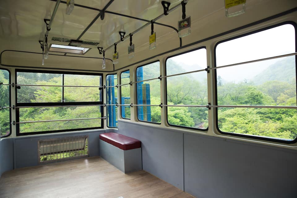 Interior de autobús con ventanas amplias, piso de madera y un banco rojo.