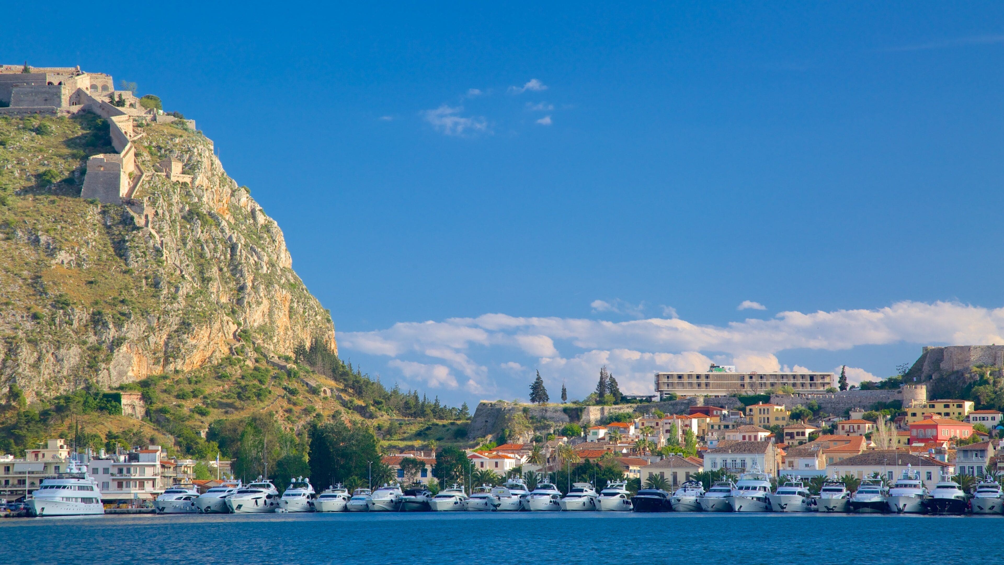 A coastal town with historic buildings, a large cliff, and a marina with boats.