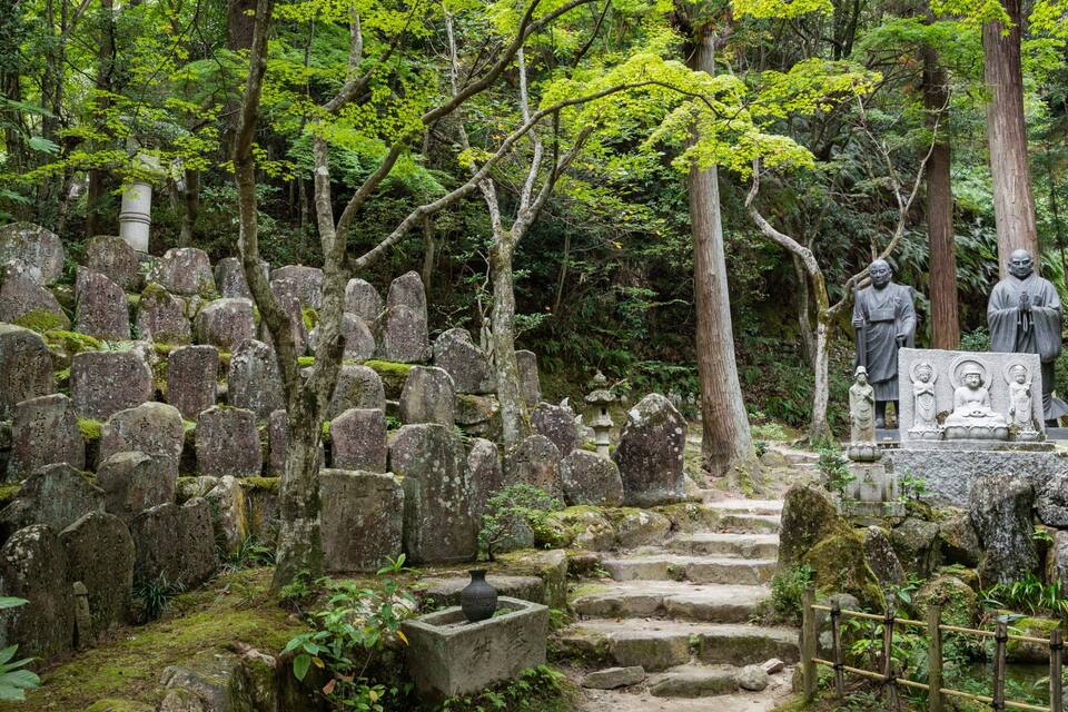A serene cemetery with stone headstones and statues in a lush forest.