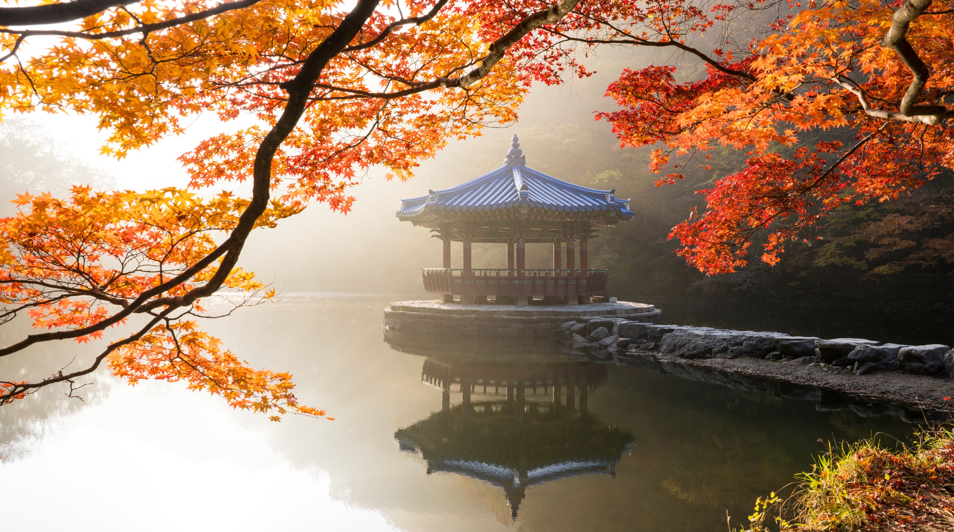 A traditional pavilion on a calm lake, surrounded by autumn foliage.