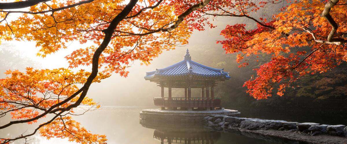 A traditional pavilion on a calm lake, surrounded by autumn foliage.