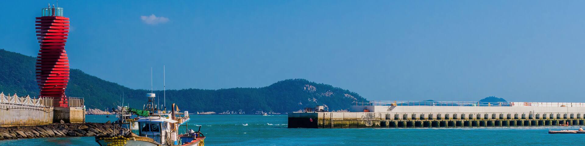 Fishing boat sailing near a vibrant red lighthouse in a harbor.
