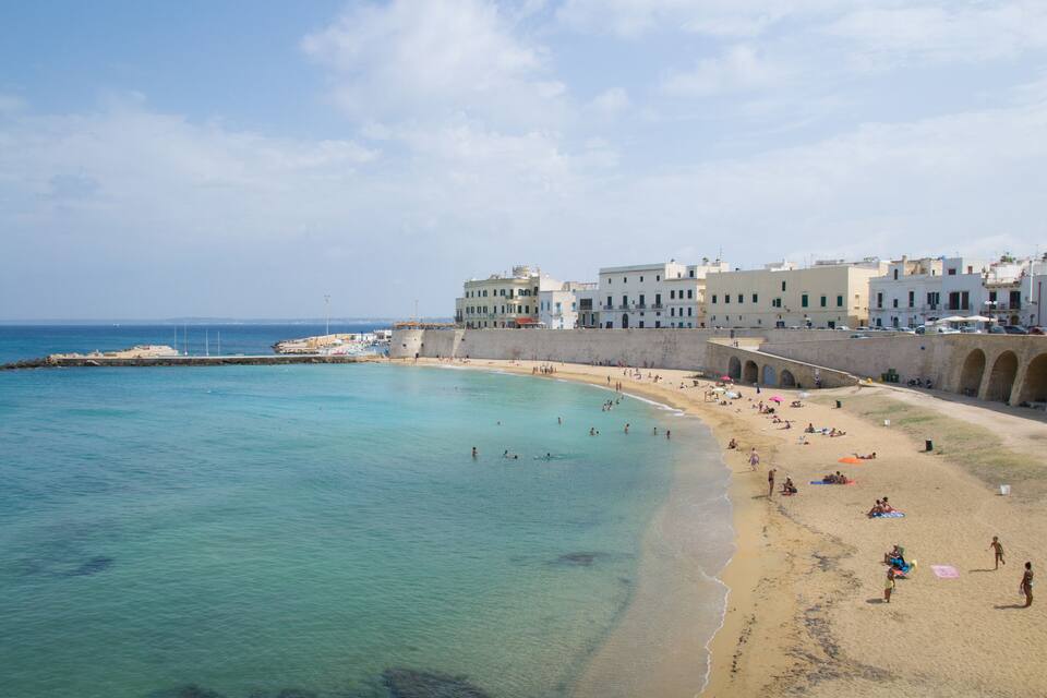 Une ville côtière dotée d’une plage de sable, d’eaux turquoise et limpides, et de bâtiments historiques qui bordent le front de mer.
