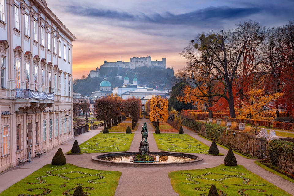 A formal garden with a statue, manicured lawns, and a castle in the background.