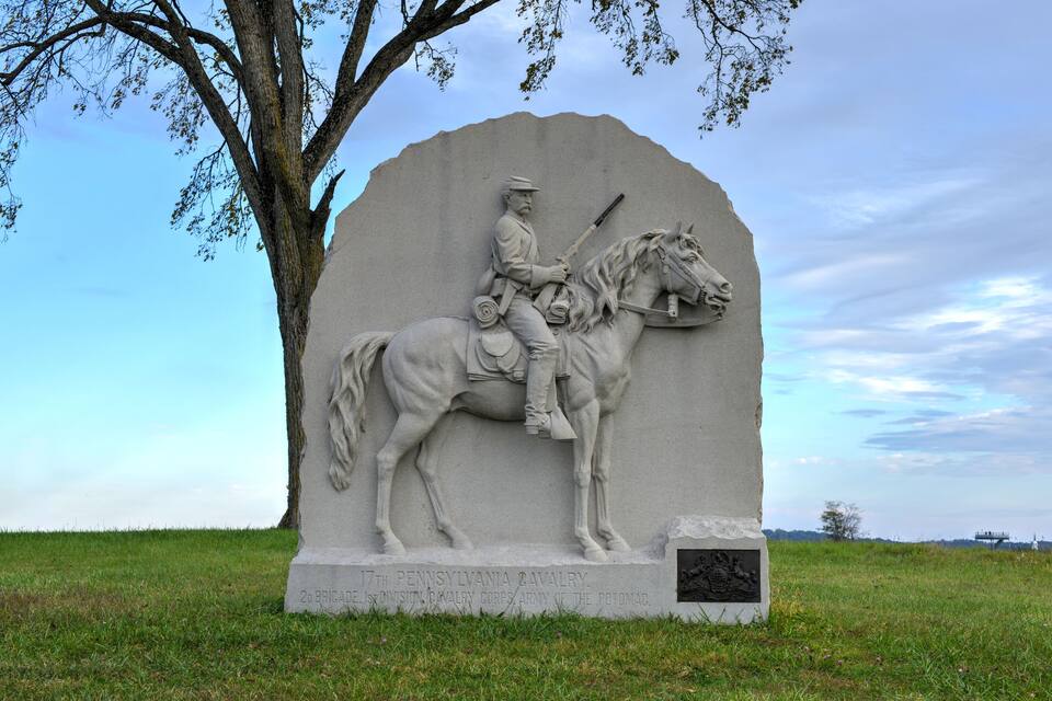Monumento de piedra de un soldado a caballo, rodeado de hierba y un árbol.
