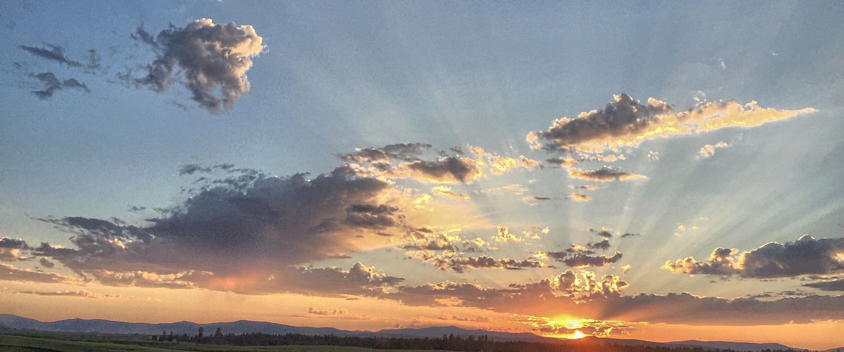 A sunset over a grassy field with scattered clouds.