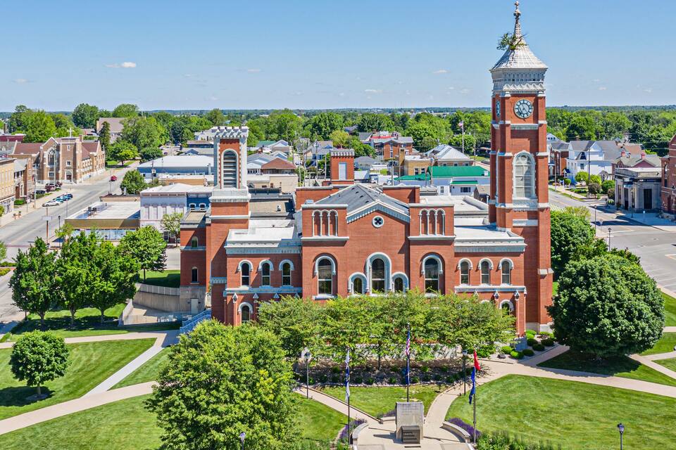 A large red brick building with a clock tower, surrounded by green lawns and trees.