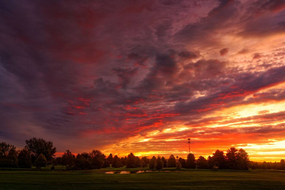 A sunset over a golf course with trees and a water body.