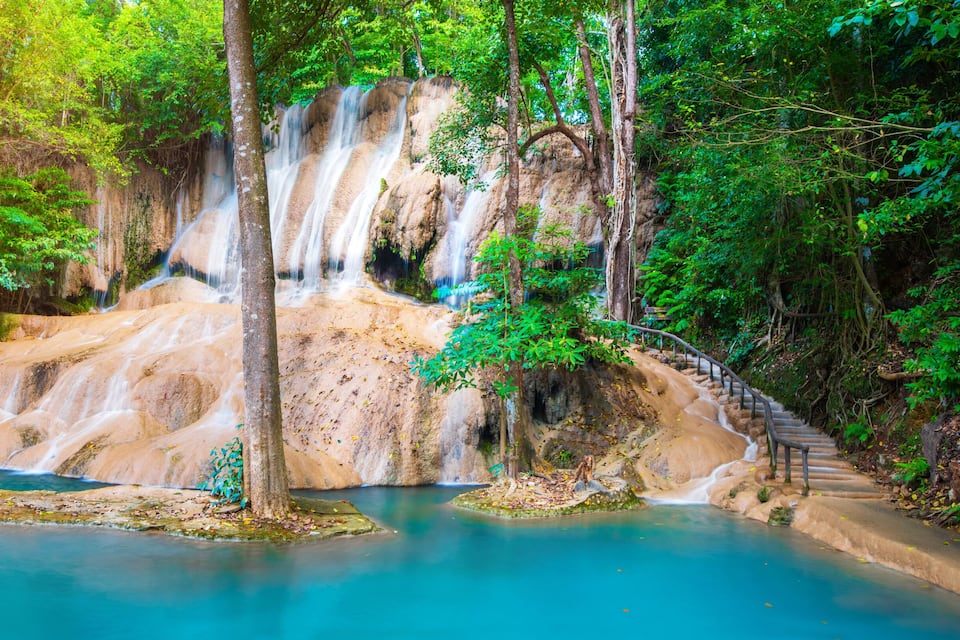 Een waterval stort neer in een turquoise poel, omringd door weelderige begroeiing.