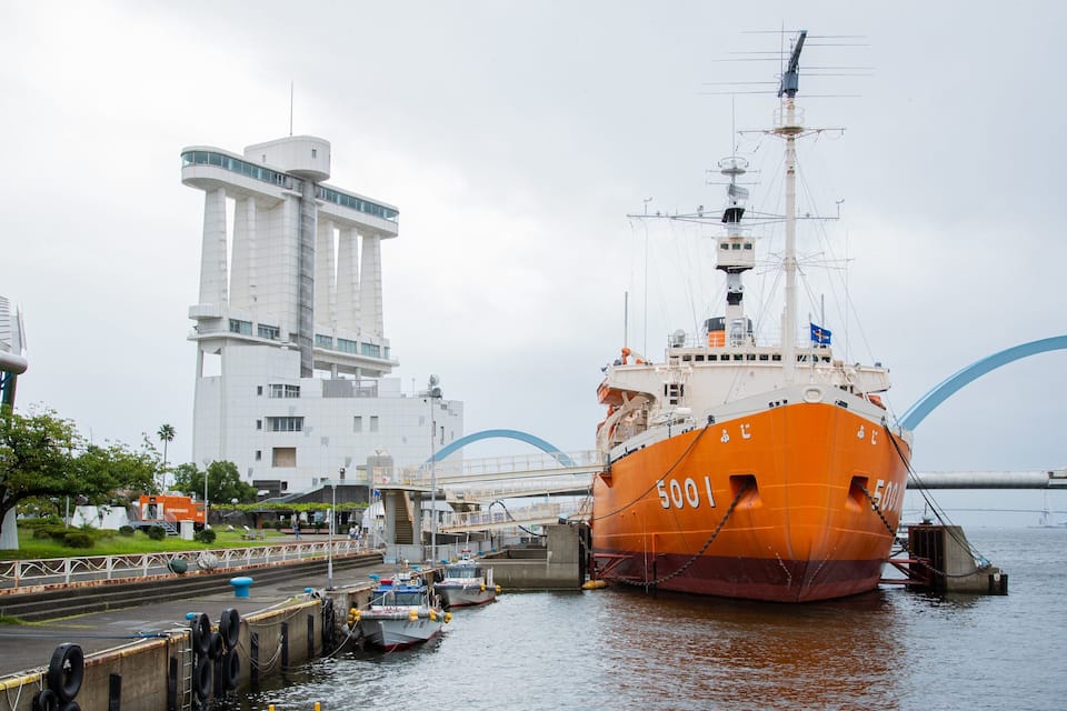 Um navio laranja grande atracado num porto, com um edifício branco moderno ao fundo.