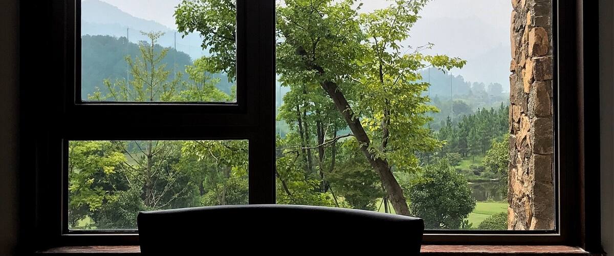 A table with a view of a green landscape through a window.