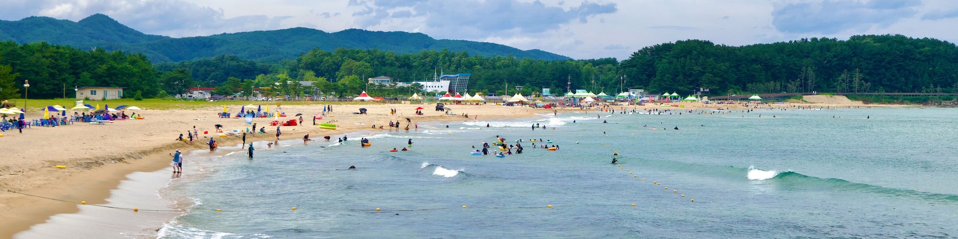 A beach with clear water, rocks, and mountains in the background.