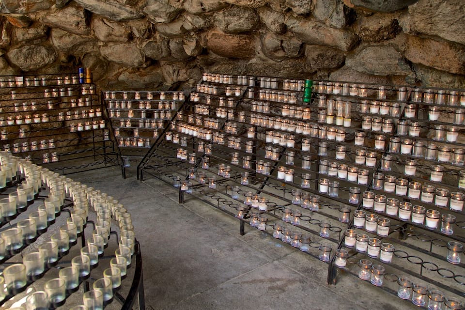 A stone-walled room filled with rows of candles on shelves.