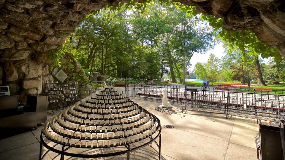A stone archway with a circular arrangement of empty glasses, a statue, and a park with benches and a fence.