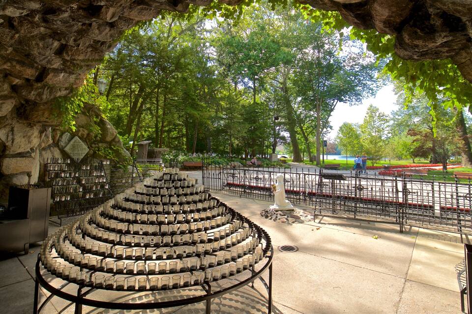 Une arche en pierre surmontée d’une disposition circulaire de verres vides, une statue et un parc avec des bancs et une clôture.