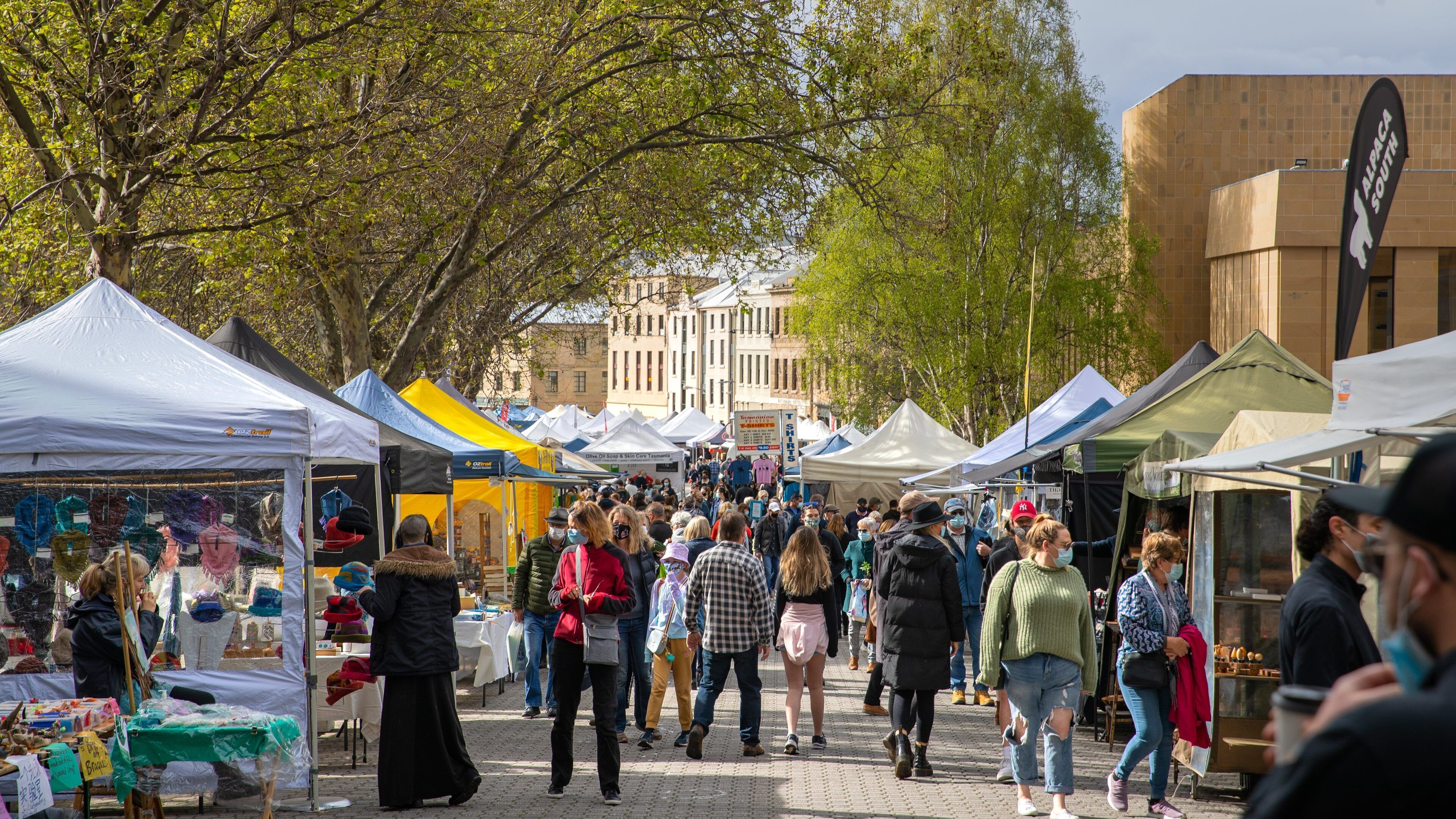 A busy outdoor market with various stalls and people walking around.