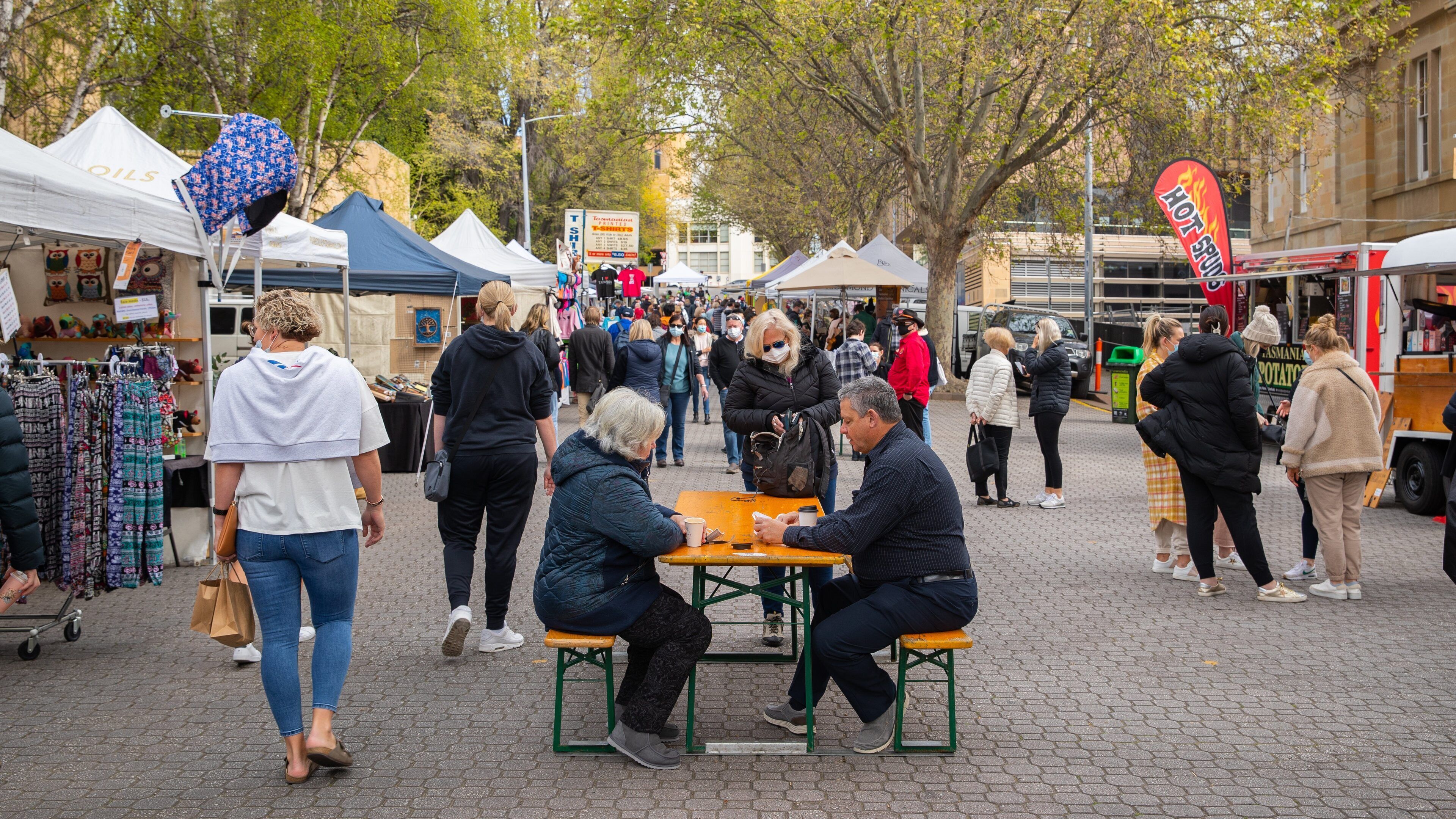 Een levendige markt in de open lucht, met mensen die lopen en aan tafels zitten.
