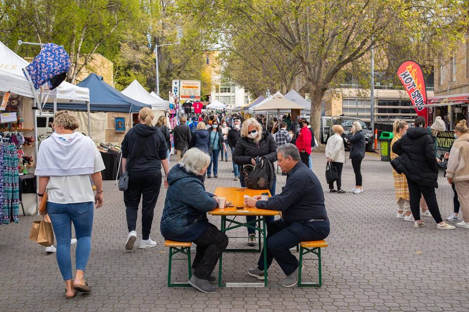 A busy outdoor market with people walking and sitting at tables.