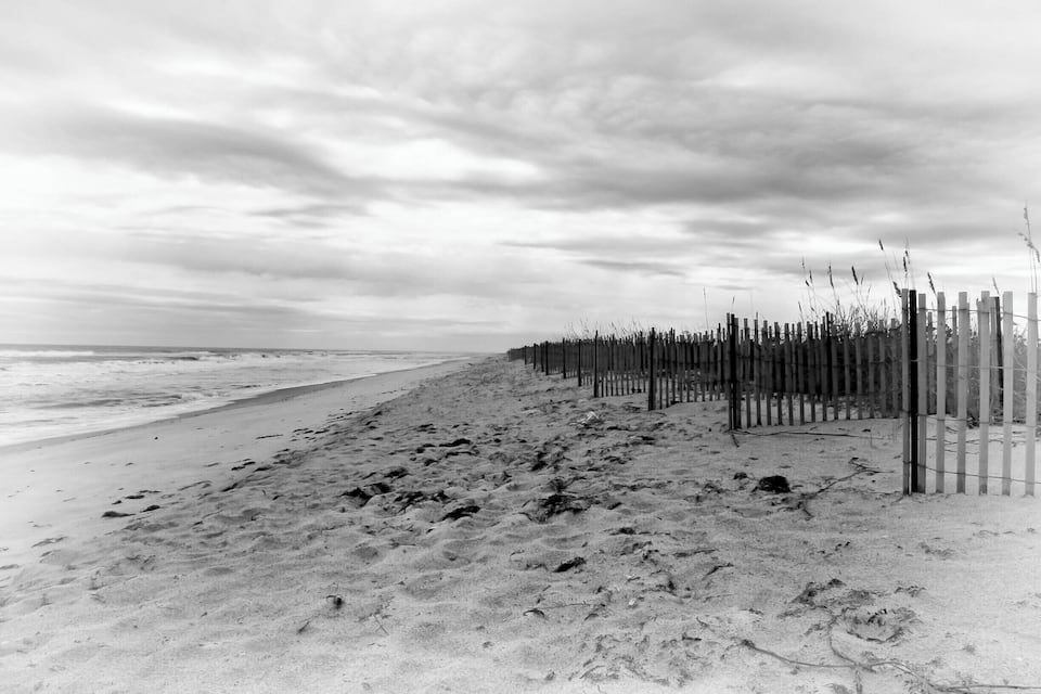 Een strand met voetafdrukken die naar een houten hek leiden.