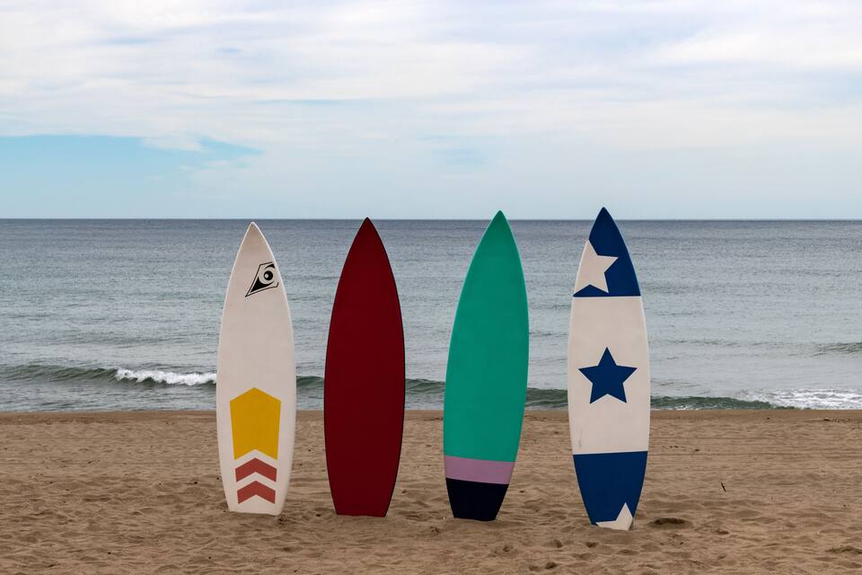 Four surfboards lined up on a sandy beach with the ocean in the background.