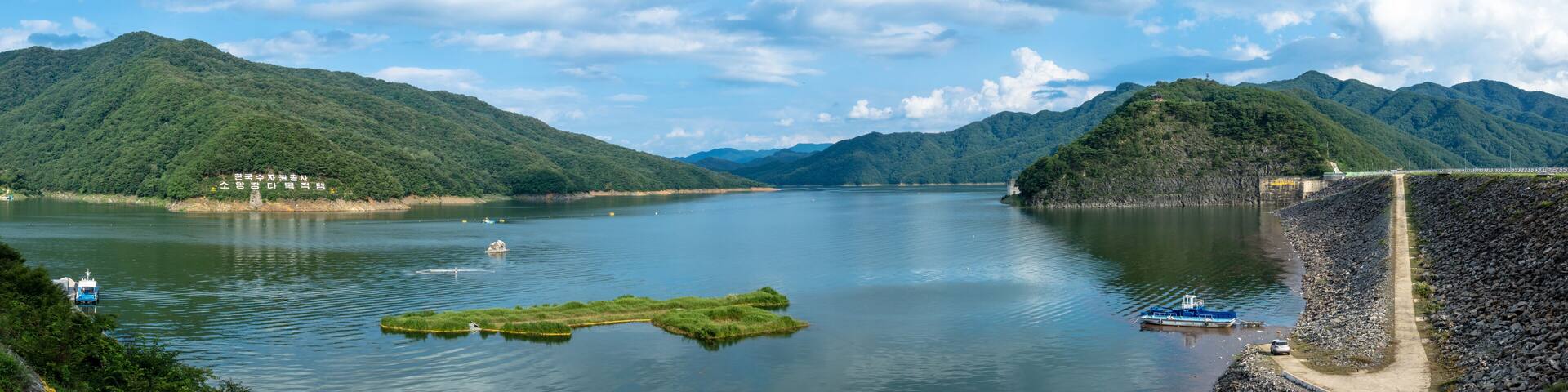 Un río con barcos, una pequeña isla y montañas al fondo.