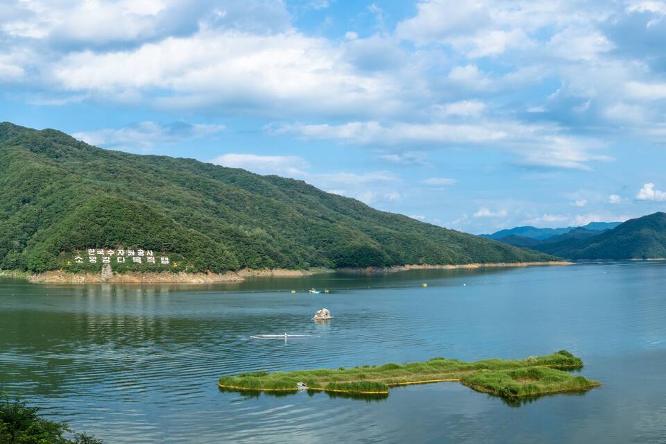 A river with boats, a small island, and mountains in the background.