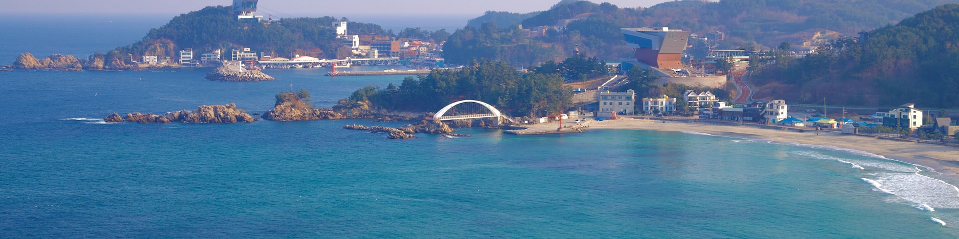 A coastal town with a prominent white bridge, rocky outcrops, and buildings on a hillside.
