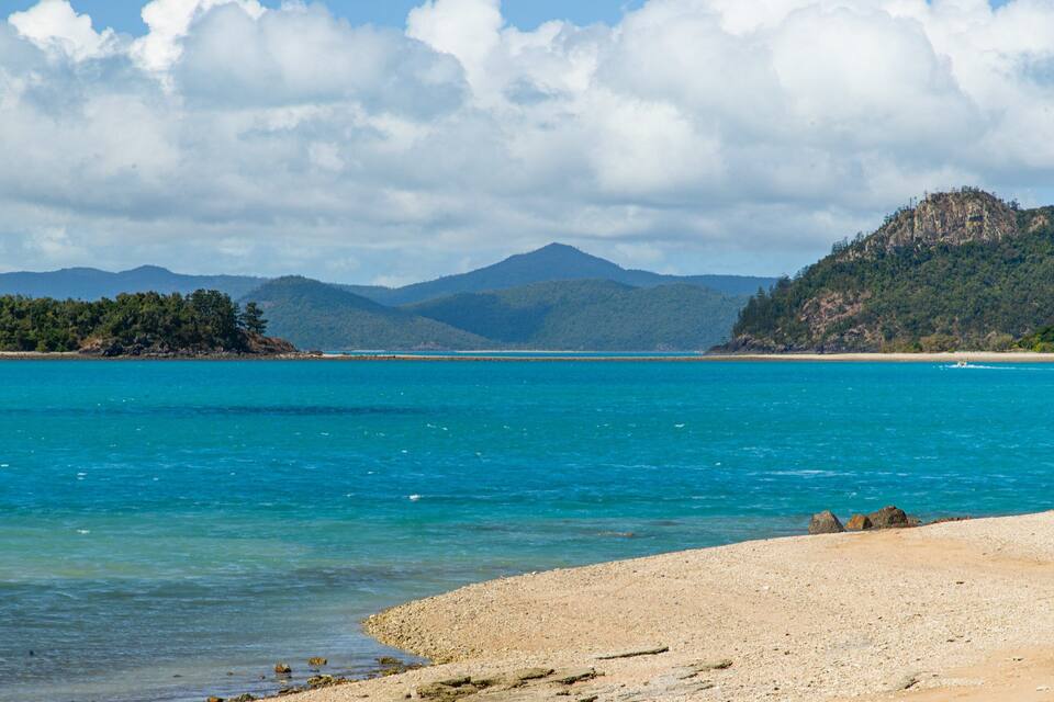 A turquoise sea, a sandy beach, and green hills in the background.
