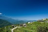 A mountainous landscape with a clear sky, a winding road, and several houses on a hillside.