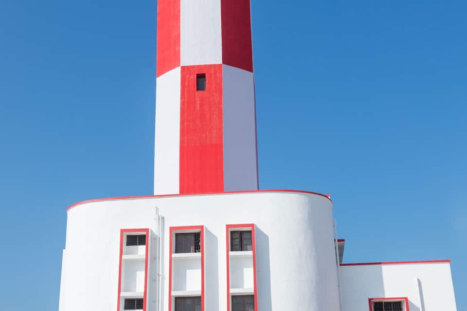 Un faro alto con franjas rojas y blancas alternadas, una base redondeada y varias ventanas.