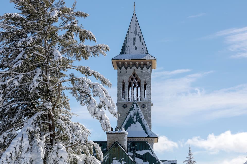 A snow-covered church tower with a pointed roof and a green roof section.
