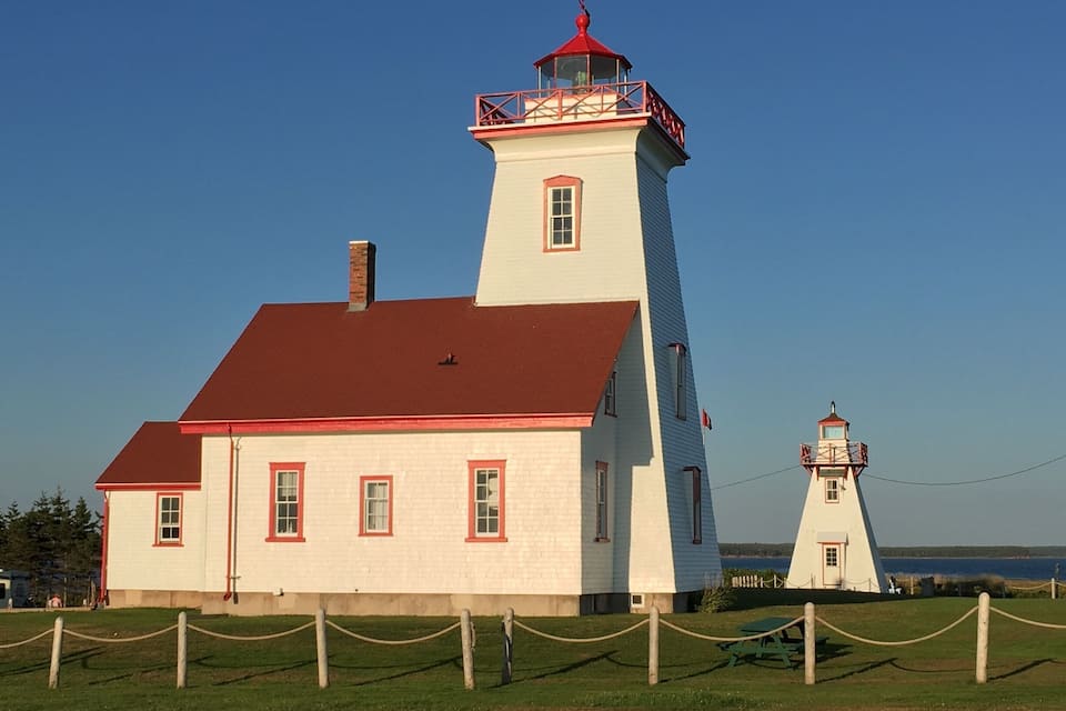 A white lighthouse with a red roof and a smaller tower, surrounded by a rope barrier.