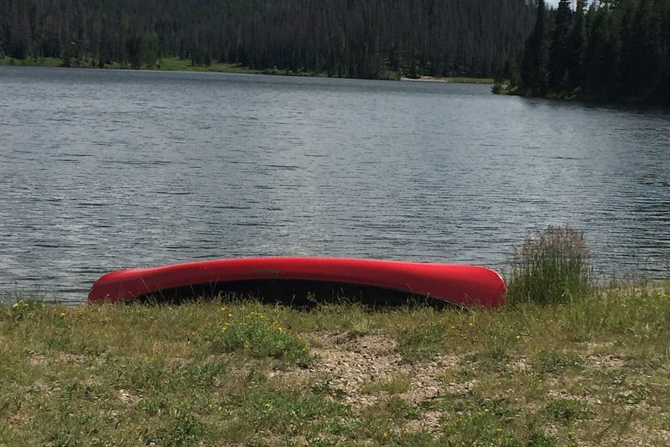 Un kayak rosso su un lido erboso, vicino a un lago con una collina boscosa sullo sfondo.