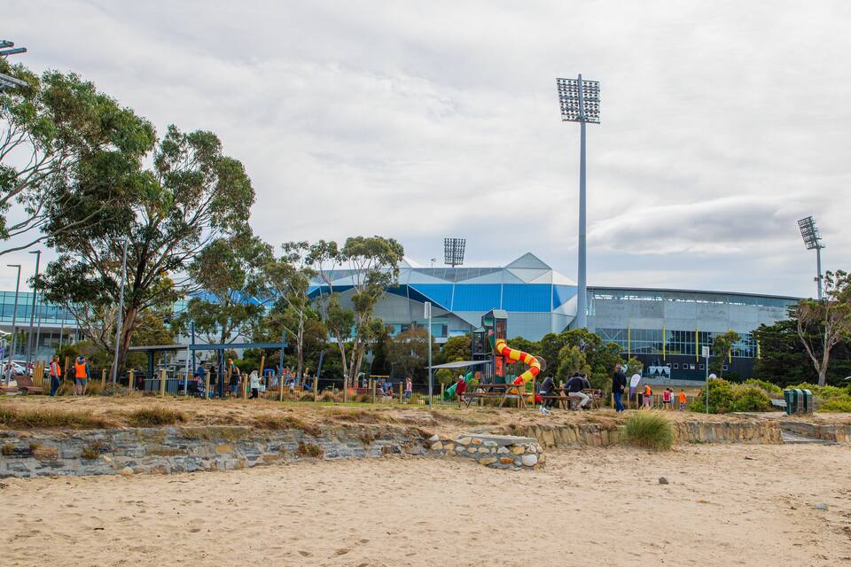 A sandy beach with a playground, trees, and a large modern building in the background.