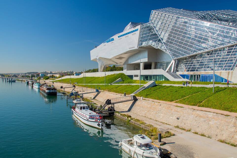 A modern architectural building with a glass facade and a river in the foreground.