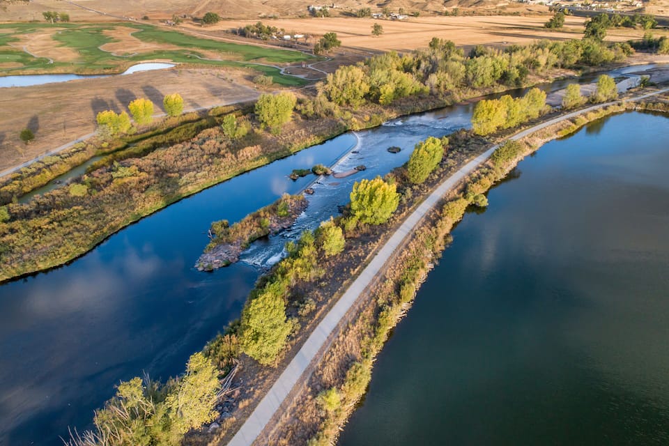 A river with a concrete path alongside, surrounded by trees and fields.